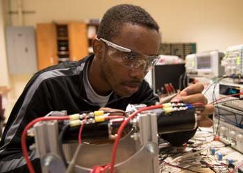 A man works on some electrical components in a room filled with electronics testing equipment