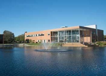 A building with large windows sits along a picturesque lake with a fountain