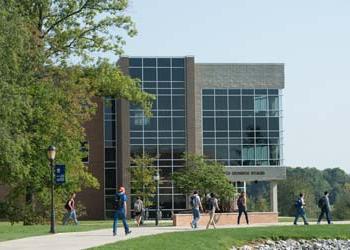 A modern building sits along a sidewalk with students walking