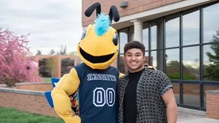 Stinger mascot posing with student outside.