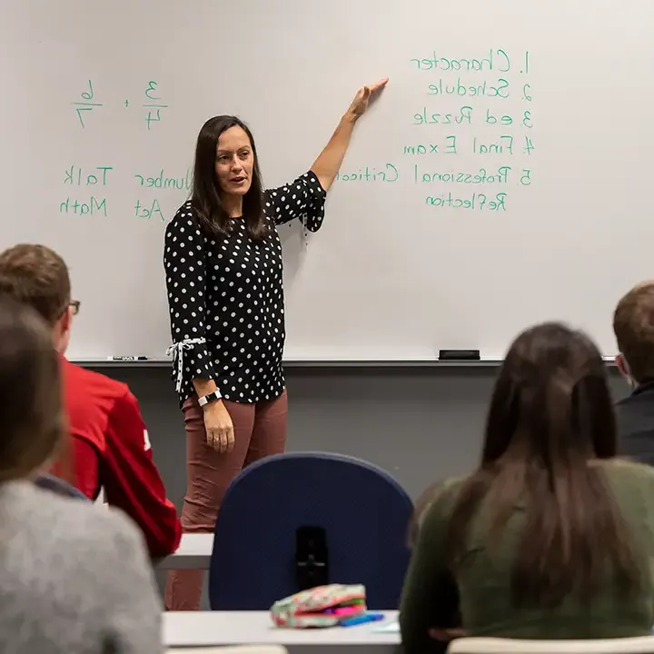 Woman standing at a whiteboard in front of seated students.